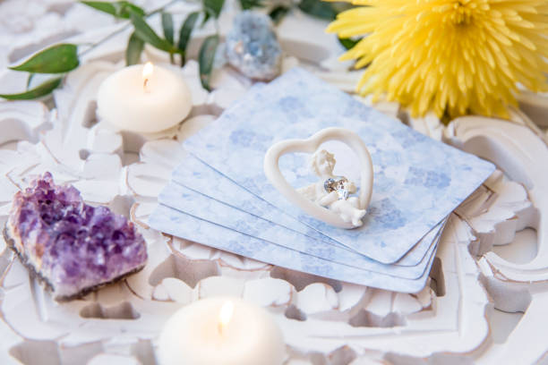 Deck with divination homemade Angel cards on bright white table, surrounded with semi precious stones crystals and candles. Selective focus on cute angel figurine. stock photo