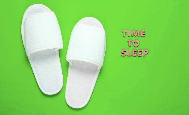 istock Time to sleep. White sleeping hotel slippers on a green background 1209487302