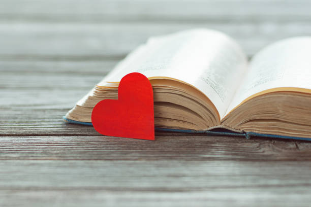 istock Open old book and red paper heart on wooden table 1209489564