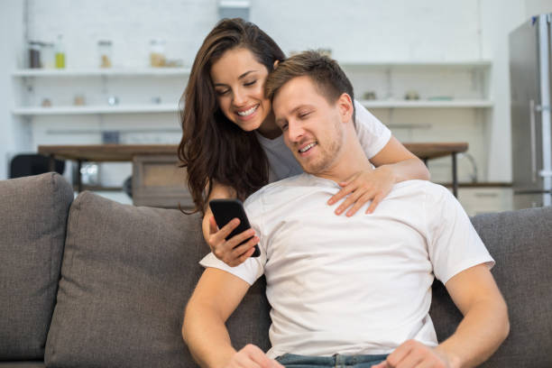 istock Smiling young couple looking at smartphone screen at home 1209489670