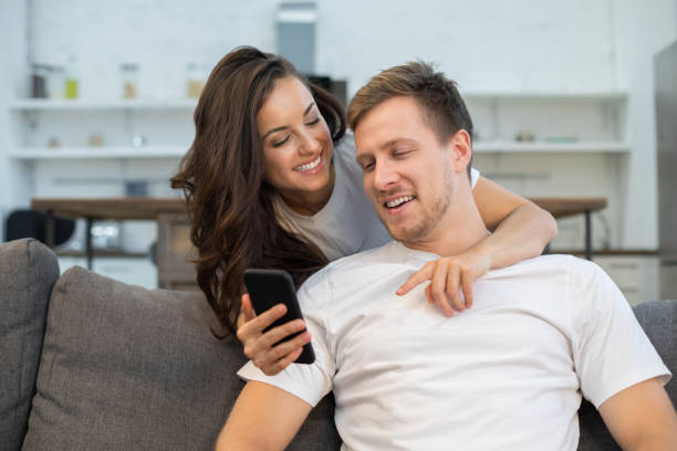 istock Smiling young couple looking at smartphone screen at home 1209489944