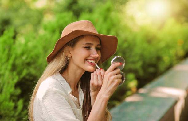 femme blonde gaie dans le modèle occasionnel utilisant des vêtements et un chapeau feutre fait le maquillage avec un revêtement de lèvre et regarde dans le miroir - lip liner photos et images de collection