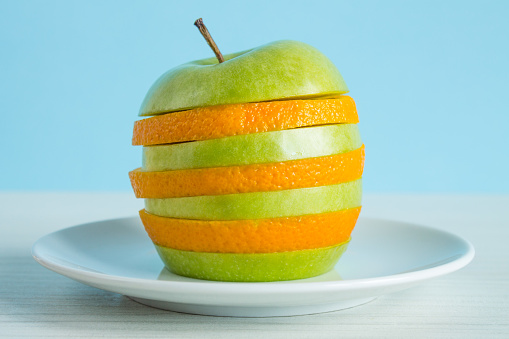 Alternating slices of apples and oranges on a white plate in close-up on a bright blue background. Concept - healthy food, vitamins, fruits, mix