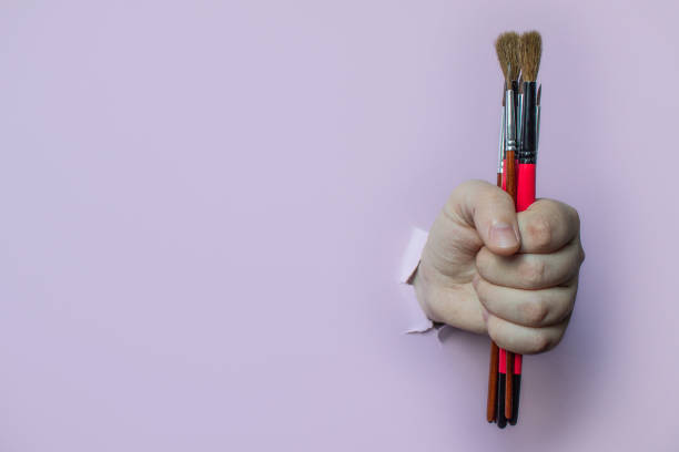 istock brushes clamped in a hand stuck through a hole in a pink background 1209494222