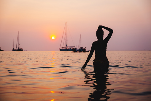 Summer travel vacation concept, Silhouette of traveler asian woman with bikini relax on sea beach at sunset in Koh Kood, Thailand