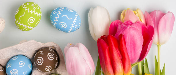 istock Painted easter eggs and bouquet of spring tulips closeup on a light blue background with space for congratulation, border design panoramic banner 1209501309