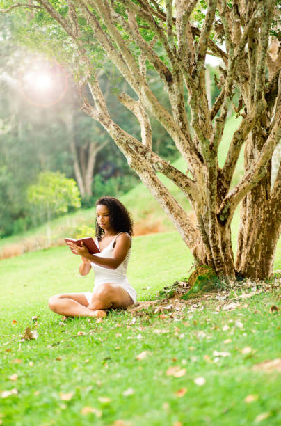 istock Young black woman reading a book in a public park 1209501822
