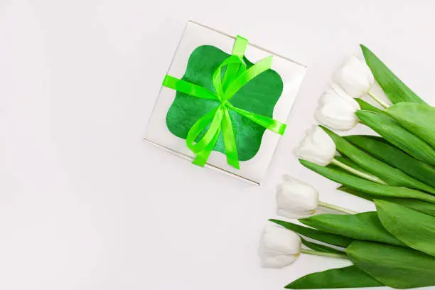 White tulip flowers and gift box with green ribbon bow on light background flat lay. Place for text 8 March Happy Womens Mothers Day.Flower Bouquet greeting card. Copy space website banner top view.