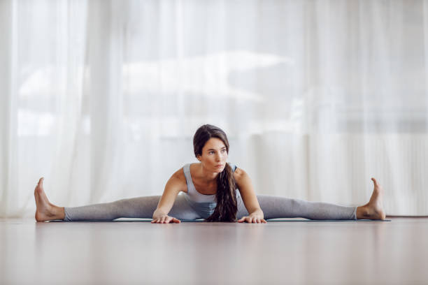 młoda atrakcyjna brunetka siedząca na macie z rozłożonymi nogami i zginająca się do przodu. koncepcja zdrowego życia. - floor women sitting yoga zdjęcia i obrazy z banku zdjęć