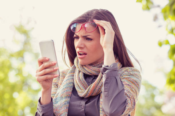 Annoyed upset woman in glasses looking at her smart phone with frustration while walking on a street on an autumn day Annoyed upset woman in glasses looking at her smart phone with frustration while walking on a street on an autumn day slander stock pictures, royalty-free photos & images