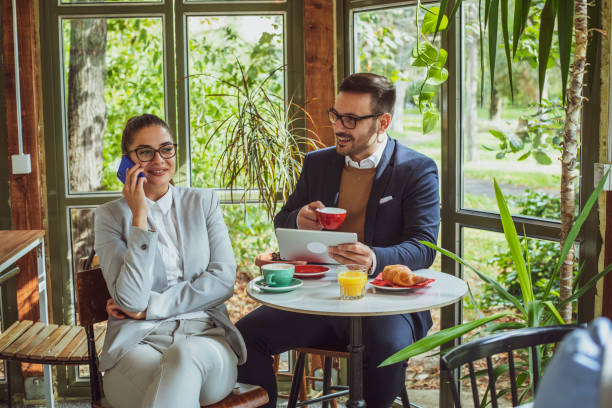 istock Two young, attractive, smartly dressed people having breakfast and coffee in a beautiful coffeehouse surrounded with greenery. 1209528000