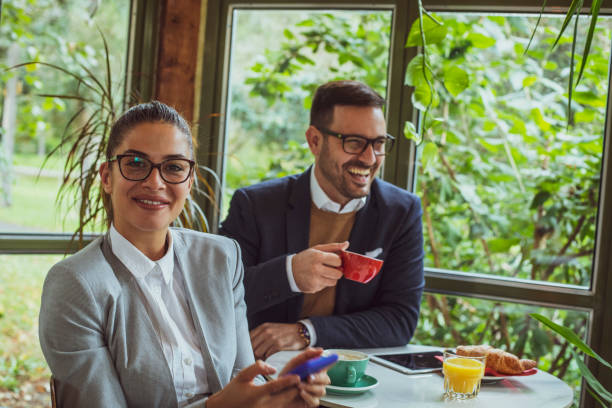 istock Two young, attractive, smartly dressed people having breakfast and coffee in a beautiful coffeehouse surrounded with greenery. 1209528001