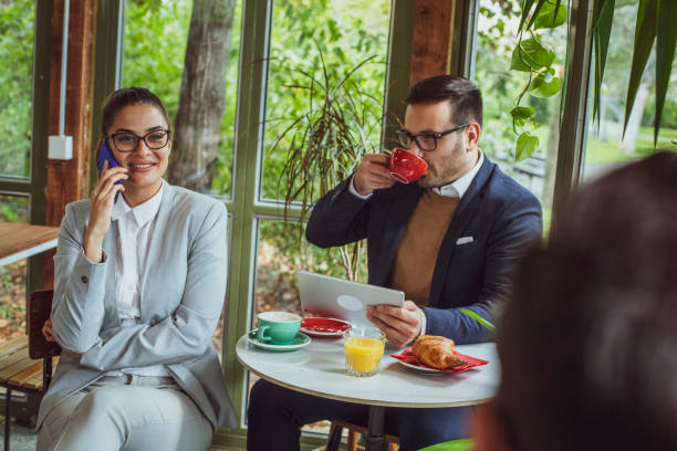 istock Two young, attractive, smartly dressed people having breakfast and coffee in a beautiful coffeehouse surrounded with greenery. 1209528003