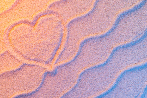Heart shape drawing on sand with wave and neon light. Minimal exotic vacation and travel concept, Flat lay top view copy space