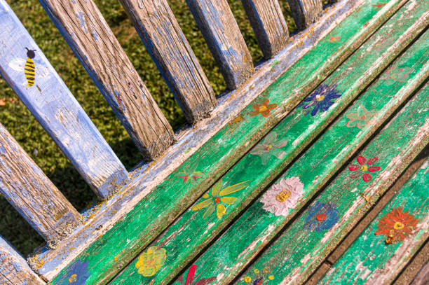 banc coloré peint à la main et altéré ou banc de parc avec des fleurs, des pétales et des abeilles dans différentes formes de couleurs dans une zone verte urbaine - dirty bench empty park photos et images de collection