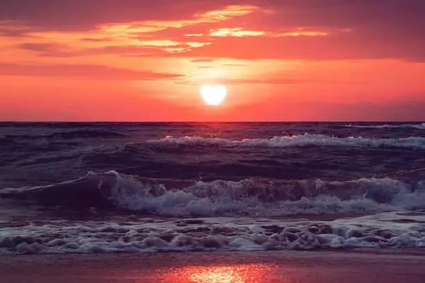 Photo of Heart walks off into the sunset over sea in dark clouds. Past love. Separation. concept. Sun is the heart is the evening before sunset. Valentine's day