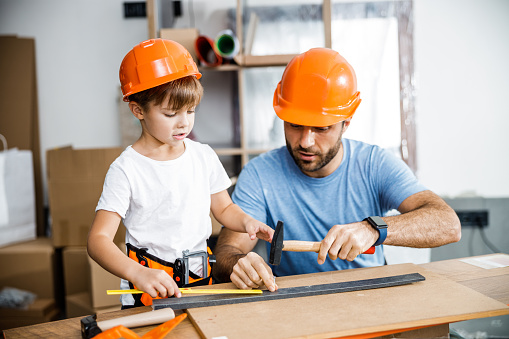 Father is spending time with son in workshop and training kid to use hand instruments on desk