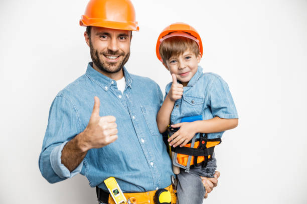 Cheerful dad is hugging little boy while they are standing with instruments in helmets and showing thumb up. Isolated on white background
