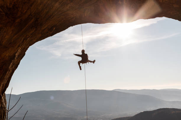 istock Male rock climber hanging on natural arch 1209559262