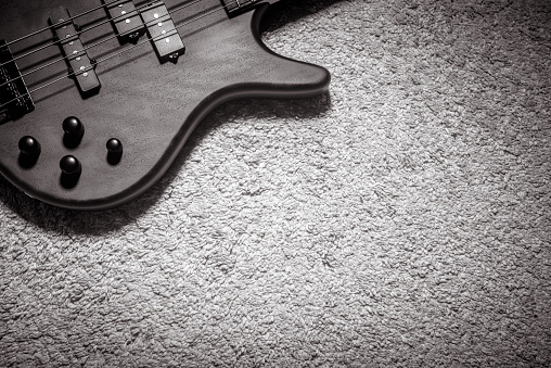 Bass guitar with four strings in black and white. Detail of popular rock musical instrument. Top view of wooden textured electric bass on carpet. Vintage style photo of bass guitar for background.