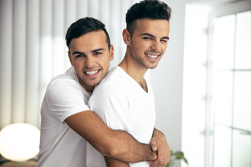 Waist up of smiling twins posing in room and looking at camera stock photo