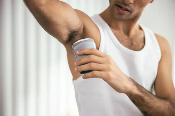 Photo of Handsome guy in t-shirt using deodorant in room