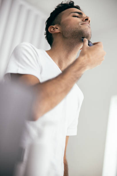 istock Young man in t-shirt trimming his beard with trimmer 1209564612