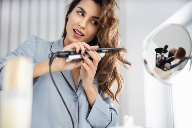 istock Happy pretty woman is using curling iron at home 1209568575