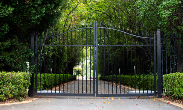 puertas de entrada de la propiedad de la entrada de hierro forjado de metal negro con exuberante sato verde y árboles de jardín - iron gate fotografías e imágenes de stock