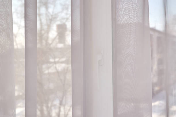 istock White tulle curtain with vertical folds. Window with light curtains. Soft textile texture. Abstract Light and shadow background. 1209603217