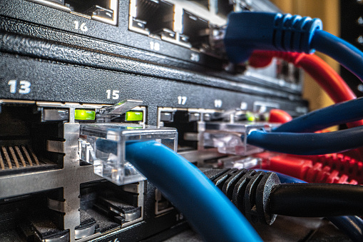 Close-Up Shot of a Blue Cat5 Ethernet Cable Connector Plugged In and Blinking Green on a Rack Mounted Network Switch Equipment Hardware in an IT Networking Closet