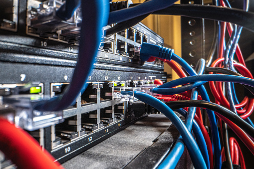 Cat5 Ethernet Cables Plugged into a Blinking Network Switch with Tangled Messy High Speed Internet Gigabit Cat6 Data Cables in the Background in an IT Networking Closet with Copy Space