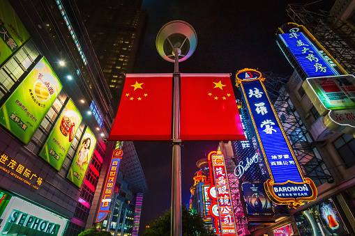 Illuminated chinese flag shot from below towards the night sky in the crowded famous Nanjing Shopping Road in downtown Shanghai. Extreme wide angle perspective for an iconic  symbolic chinese consumerism concept photo. Nanjing Road, Shanghai, China, Asia.