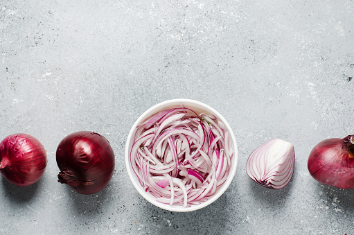 Pickled chopped red onion in vinegar in a white plate. Whole and sliced onions. A delicious side dish for meat and fish dishes. Light grey background. Flat top view. Copy space