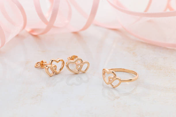 Jewellery set of hearts shape rose gold ring and stud earrings on pink background stock photo