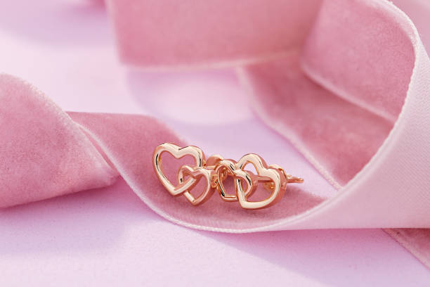 Hearts shape rose gold stud earrings on pink background stock photo