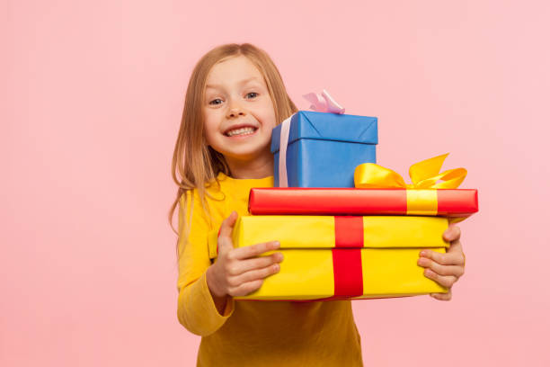Delighted little girl embracing lot of gift boxes and smiling at camera with expression of sincere childish happiness Delighted little girl embracing lot of gift boxes and smiling at camera with expression of sincere childish happiness, enjoying perfect birthday with many presents. indoor studio shot, pink background birthday present stock pictures, royalty-free photos & images