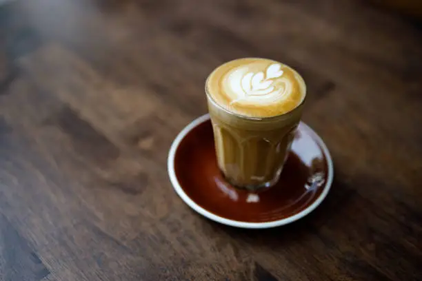 Photo of small cup of coffee with heart pattern froth on wooden table