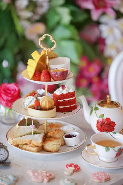 Afternoon tea. A traditional British afternoon tea party in Wonderland concept with selective focus on the red velvet heart cake. Sugar glazed cookies in fairy tales concept are scattered on the table.