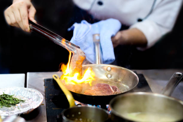 istock Chef cooking with flame in a frying pan on a kitchen stove 1209637418