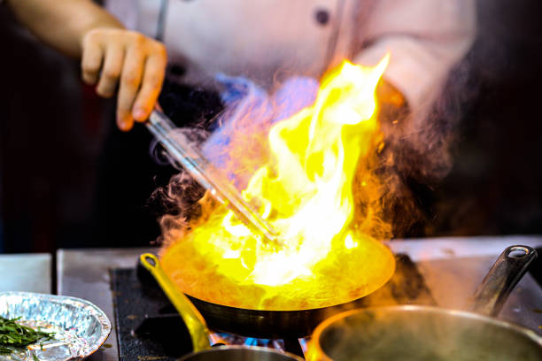 istock Chef cooking with flame in a frying pan on a kitchen stove 1209637425