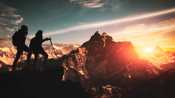 히말라야 산맥의 정상에 올라 올라가는 젊은 아시아 커플 등산객. 서로를 돕는 사람들은 일출에 산을 하이킹. 도움의 손길을 내미는다. 등반, 도움 및 팀 작업 개념 - climbing achievement leadership adventure 뉴스 사진 이미지