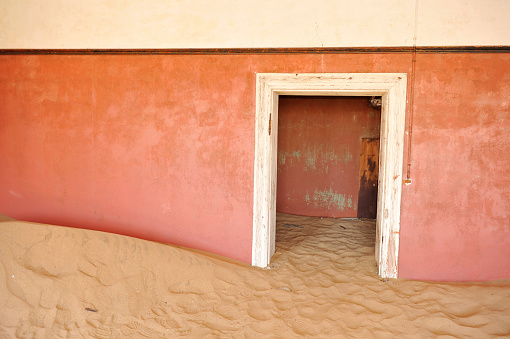 Sand from the Namib desert is blown up against an orange wall of an abandoned house in Kolmanskop,a ghost town in the restricted diamond mining area near Luderitz,Namibia.