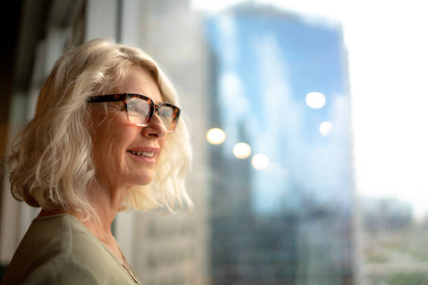 imprenditrice matura che guarda fuori dalla finestra - looking through window window business women foto e immagini stock