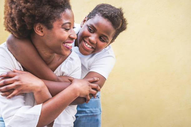 happy young mother having fun with her kid - son hugging his mum outdoor - family connection, motherhood, love and tender moments concept - focus on boy face - child caribbean black latin american and hispanic ethnicity imagens e fotografias de stock