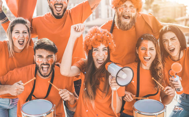 los aficionados al deporte naranja gritando mientras apoyan a su equipo fuera del estadio - aficionados al fútbol que se divierten en el evento de competición - campeones y concepto ganador - enfoque en la cara de la chica del centro - orange white audio fotografías e imágenes de stock