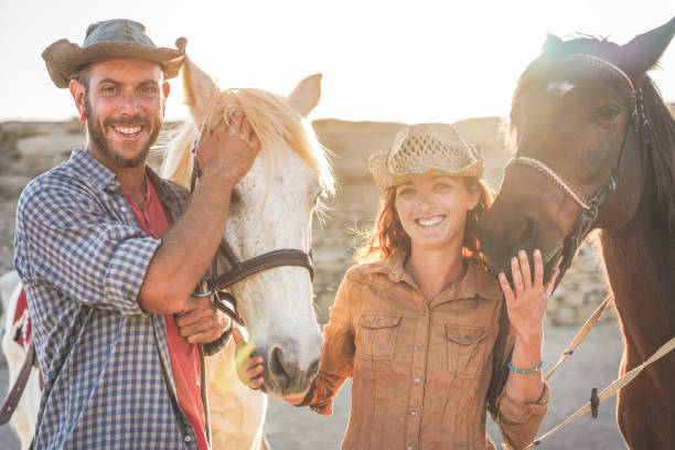 istock Animals lovers couple taking with bitless horses during sunny day inside ranch corral - Happy people having fun training at their farm - Love and wild concept - Focus on guys faces 1209660414
