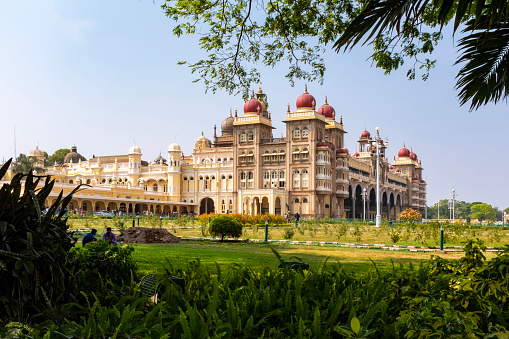 Trees framing a view of the Mysore palace with unrecognisable people far in the background, India