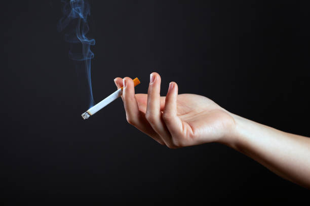 beauty hand of a girl with a cigarette and white smoke on a dark black background stock photo