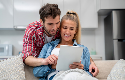 Happy couple at home browsing online on a digital tablet and smiling - lifestyle concepts
